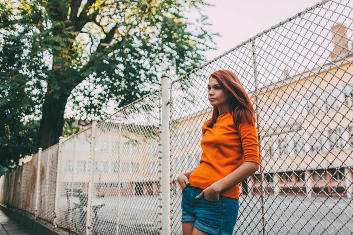 Portrait of a woman leaning on a fence outdoors.