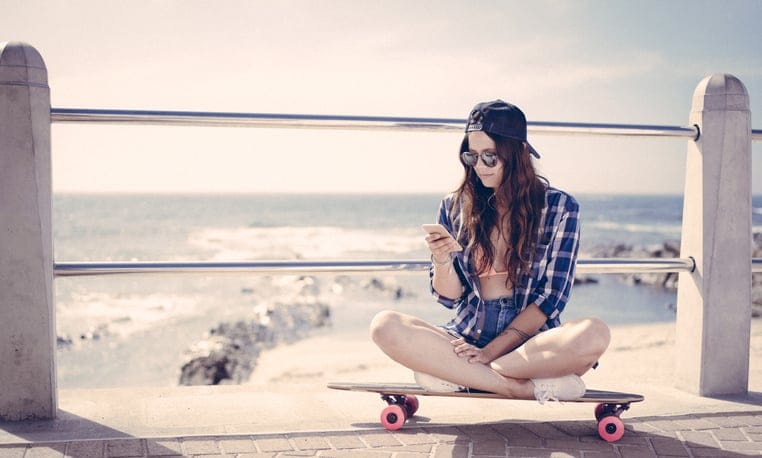 Skater girl checking her phone while sitting on her skateboard