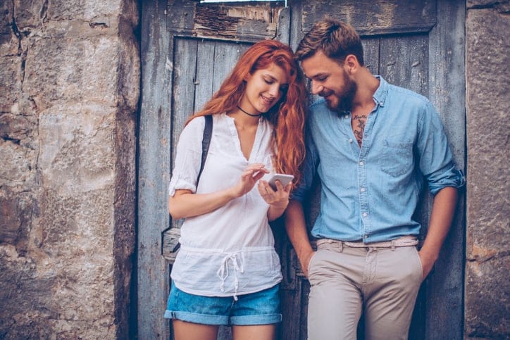 Young tourist couple, exploring foreign city. Standing by old doors and checking digital map. Wearing casual clothes and backpacks.