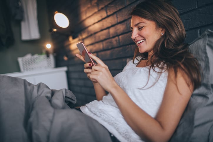 Young, smiling woman using smart phone in the bed