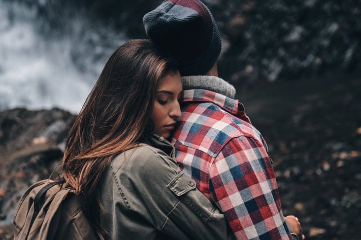 Young attractive woman embracing her boyfriend while standing near the waterfall