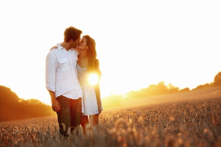 An affectionate young couple walking through a field holding each other