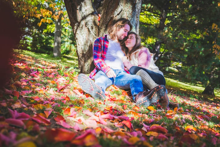 Couple getting cozy under a tree during their visit to local park in fall