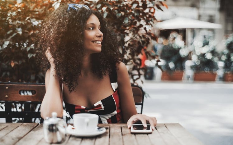 Curly laughing woman in a street cafe with the cellphone