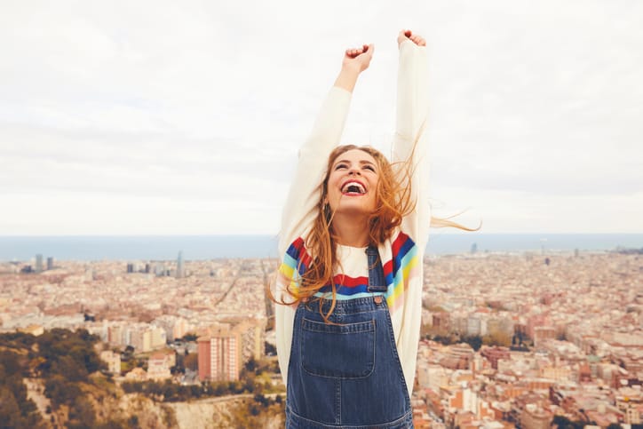 Happy woman with arms raised against cityscape