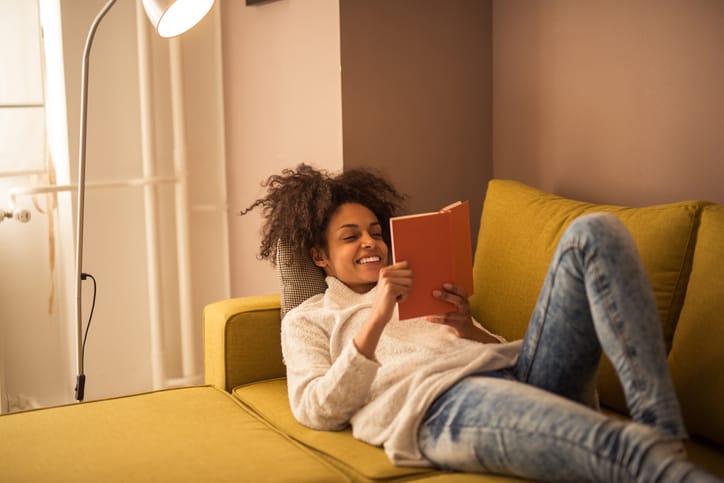 An introverted young woman home alone and reading a book while lying on the sofa in the living room