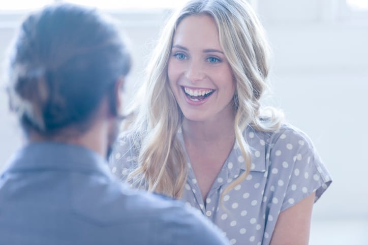 Business colleagues having a conversation. They are both young business people casually dressed in a bright office. Could be an interview or consultant working with a client. She is listening and smiling One person has his back to us. He has a beard and both are casually dressed.