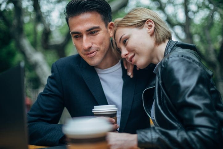 Young happy couple sitting in coffee shop and using laptop