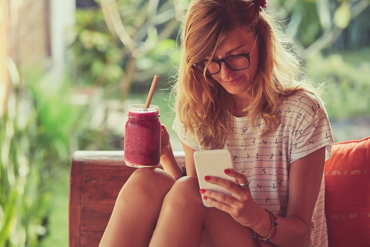 Beautiful woman using cellphone while drinking smoothie outdoors.