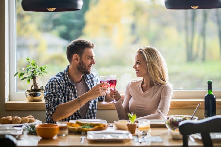 Happy couple toasting with red wine during lunch time at home.