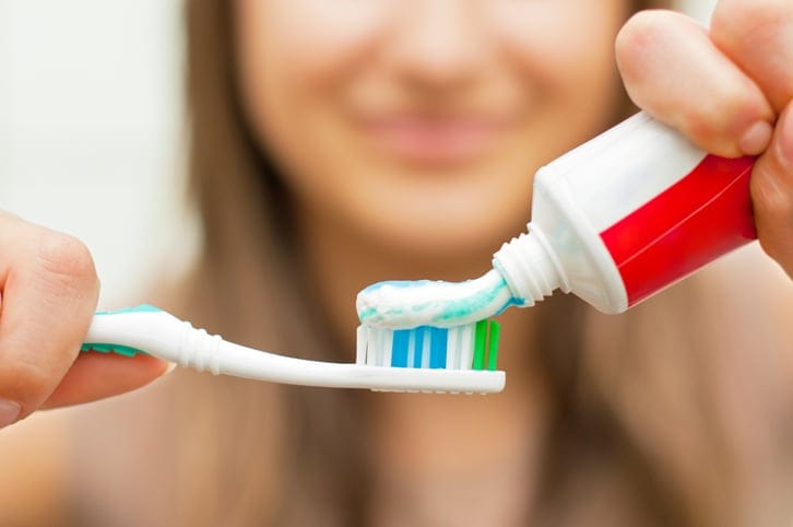 Woman putting toothpaste on a toothbrush.