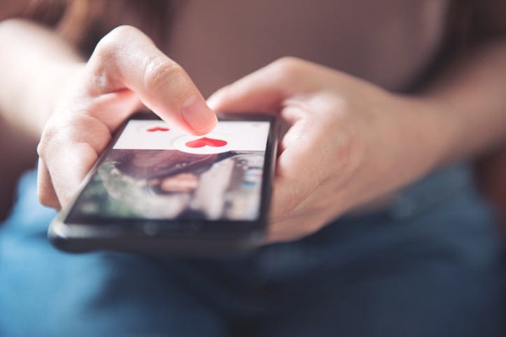 Finger of woman pushing heart icon on screen of smartphone.