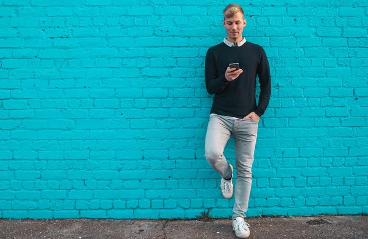 Young man standing against wall and checking phone