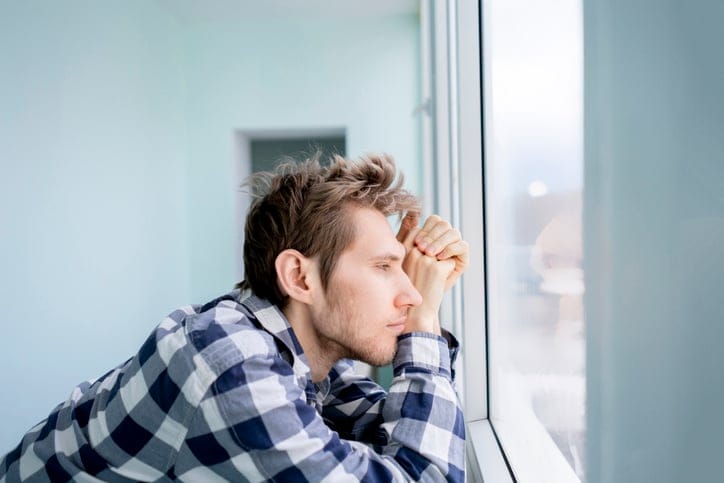 bored young man feeling sad and standing in front of the mirror
