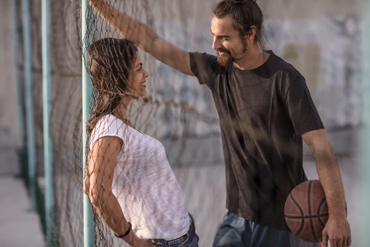 beautiful, casualy dressed sports couple flirting and hanging out on the asphalt basketball court on a sunny day at the end of the summerbeautiful, casualy dressed sports couple flirting and hanging out on the asphalt basketball court on a sunny day at the end of the summer