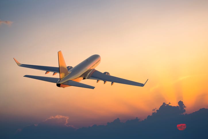 Passenger airplane flying above clouds during sunset.