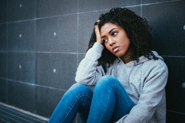 sad woman with head in hands against wall