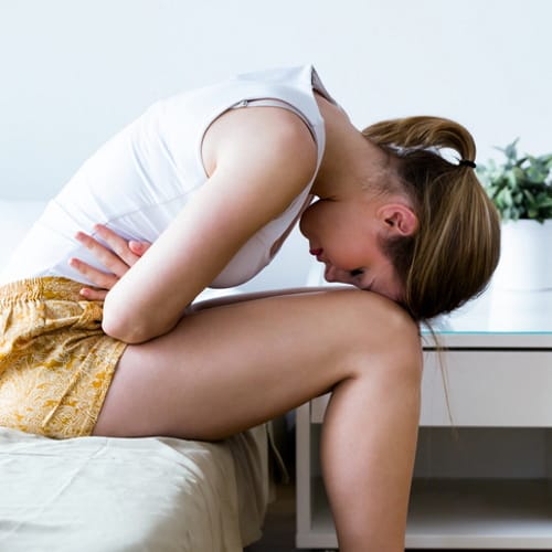woman in pain bending over bed