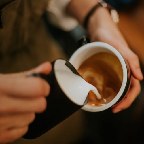 Frothy milk going into a coffee cup.