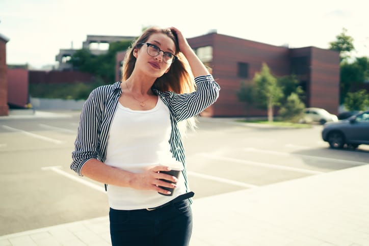 Beautiful young woman dressed in stylish outfit posing for camera while strolling around city with coffee at leisure time.Pondering good looking student enjoying recreation at street with aroma drink