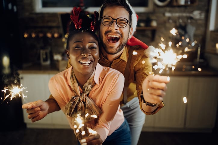 Young cheerful couple having fun with sparklers on New Year's eve at home.