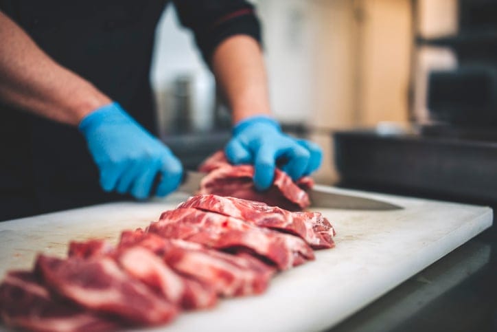 Male butcher cutting raw meat.