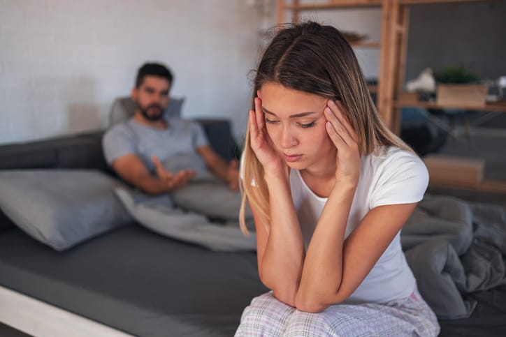 signs your relationship is over Beautiful depressed woman sitting on bed while her angry boyfriend yells at the background