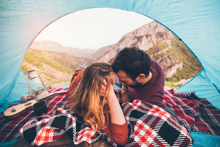 Portrait of loving couple camping in nature on autumn day, having their favourite things: cup of coffee, ukulele and each other