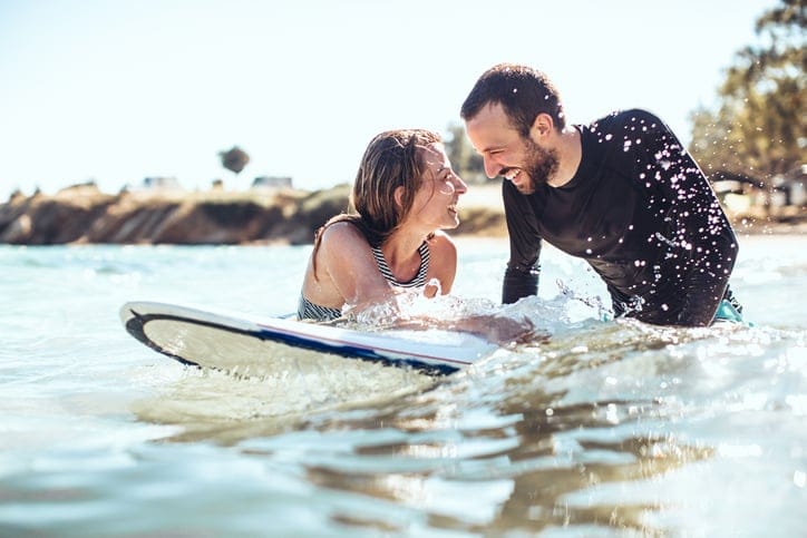 signs a man is falling in love Loving couple of smiling surfers in the water, flirting while waiting for a good wave to come