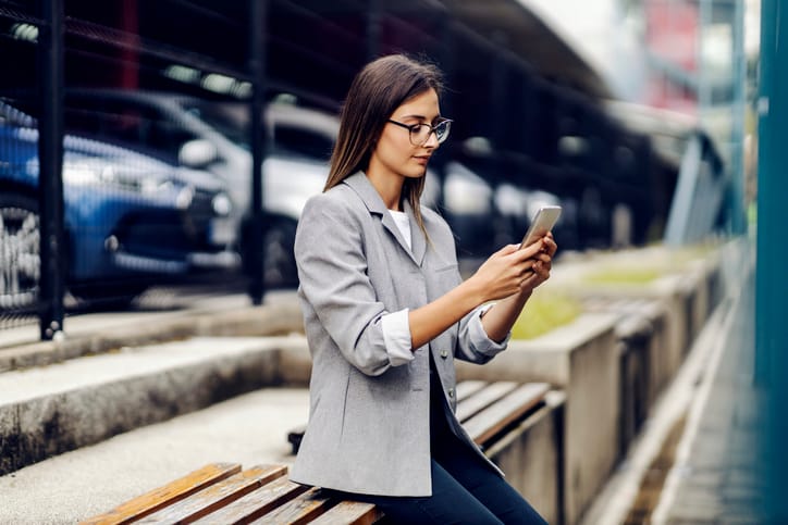 A successful young businesswoman dressed smart casual is sitting outdoors and replying messages to a satisfied client. Nowadays, everywhere is our workplace.