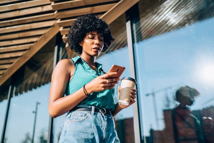 serious woman texting while walking with coffee