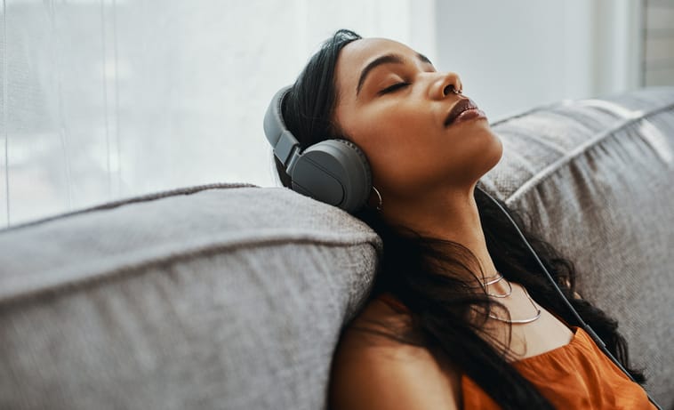 Young woman using headphones while relaxing on the sofa at home.