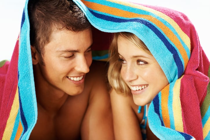 Young couple lying together under towel at the beach.