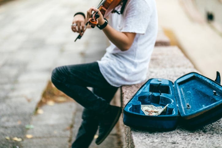 Young man playing violin outdoor for money.
