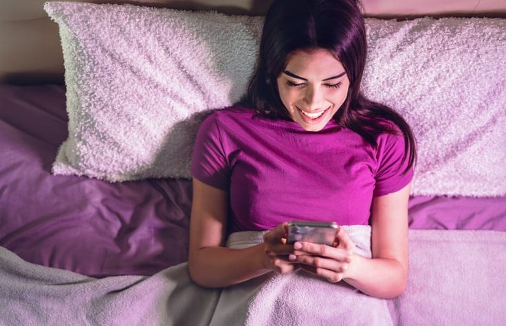woman laid in bed with smartphone