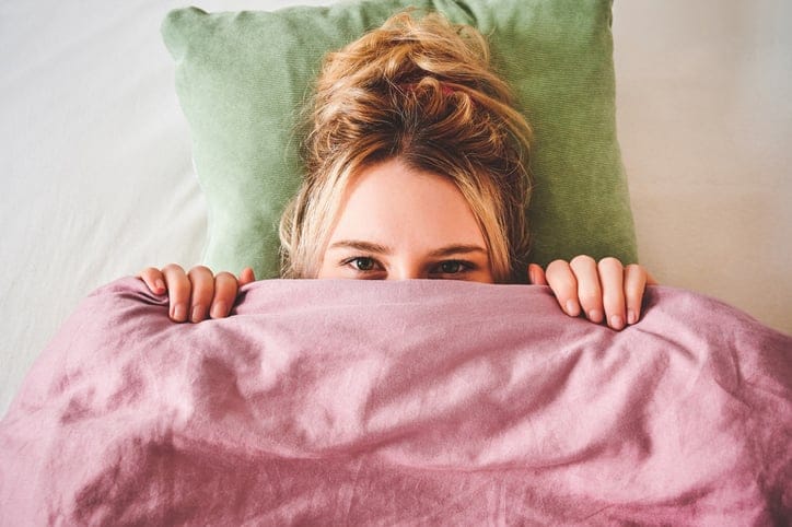woman peeping over bed covers