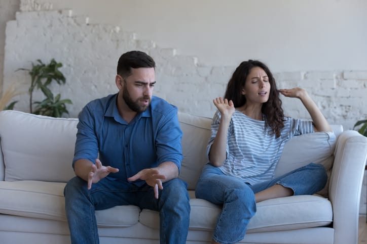 A couple sitting on the couch and quarreling, the woman shows a lack of empathy towards the man