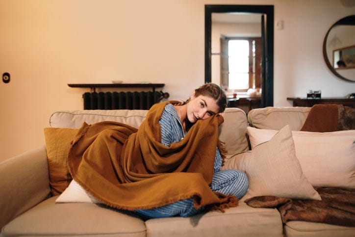 Young woman with a blanket sitting on sofa.