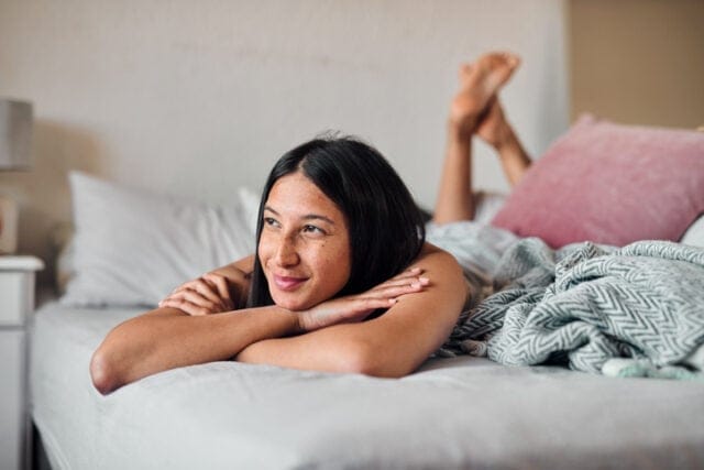 happy young woman looking thoughtful in bed