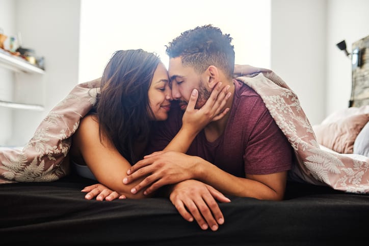 couple kissing under covers in bed