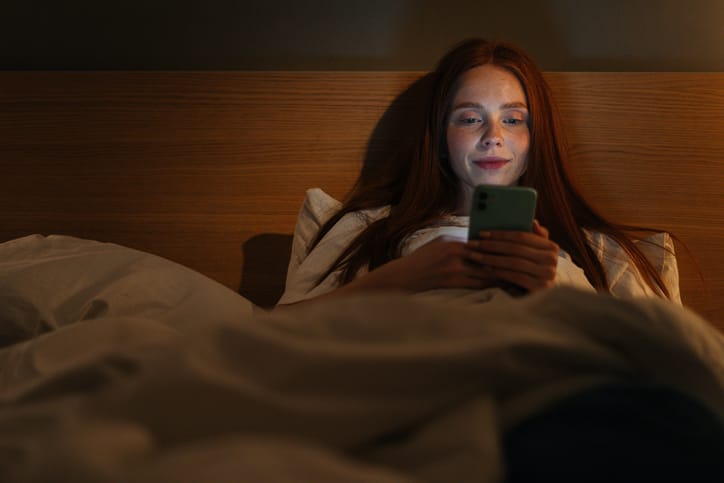 smiling woman texting in bed
