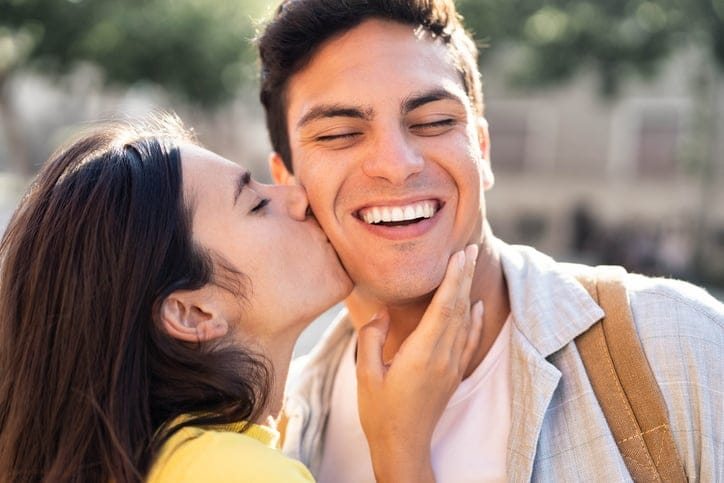 woman kissing laughing man on cheek