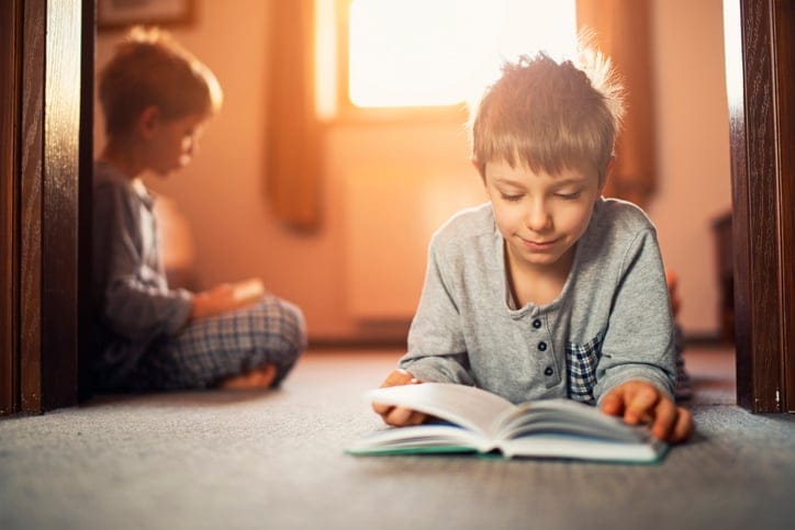 Siblings reading books on the floor.