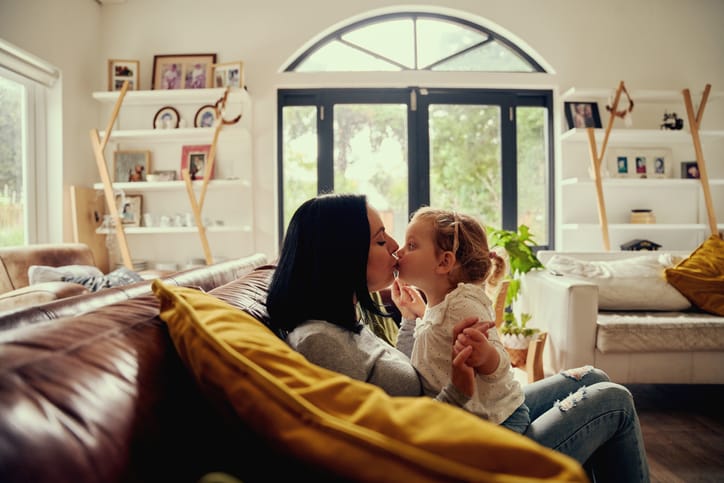 Mom kissing daughter on couch.