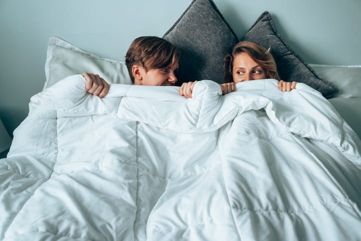 Shy couple smiling in bed.