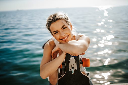 smiling blonde woman skateboard sea