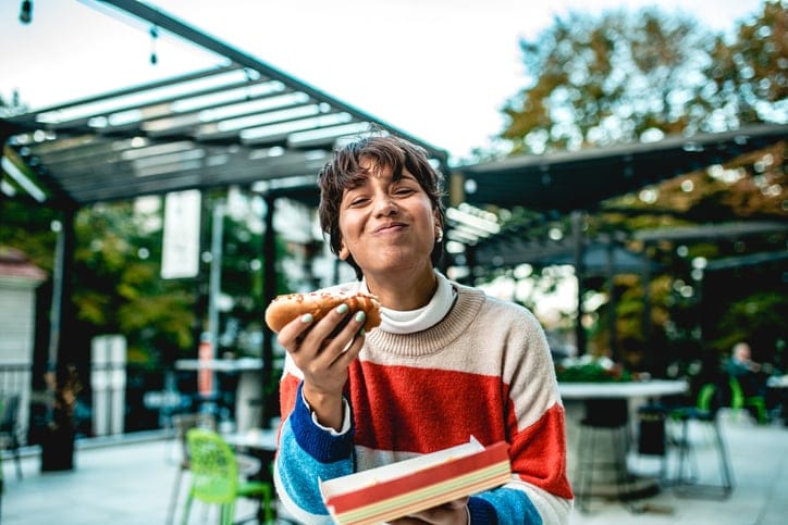 Smiling woman eating hot dog.