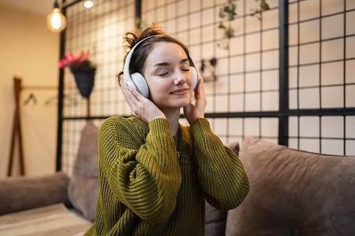 one woman adult caucasian female using headphones for online guided meditation practicing mindfulness yoga with eyes closed on the sofa bed at home real people self care concept copy space