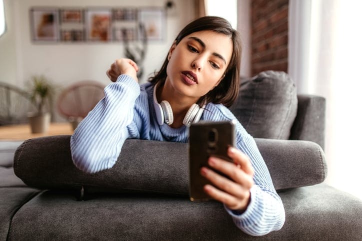 Woman texting on couch with headphones.