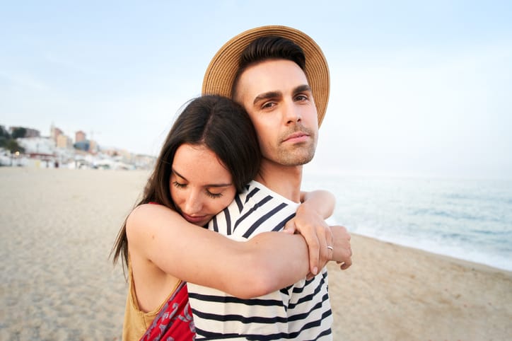 woman hugging boyfriend from behind on beach